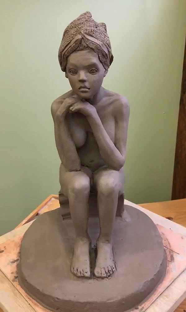Clay sculpture of a seated figure.