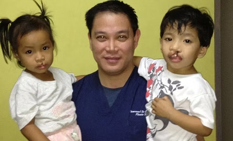Doctor holding two children, warm smile.