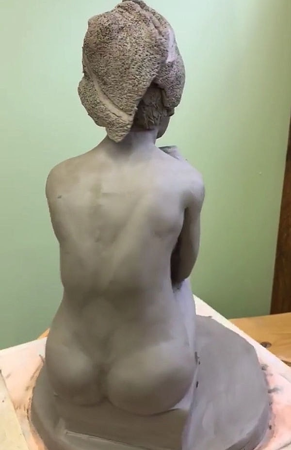 Clay sculpture of a seated figure's back.