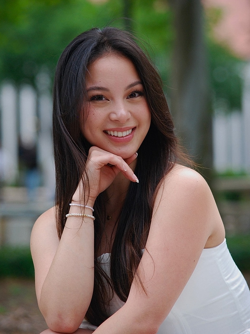 Smiling woman in outdoor setting, wearing white dress.