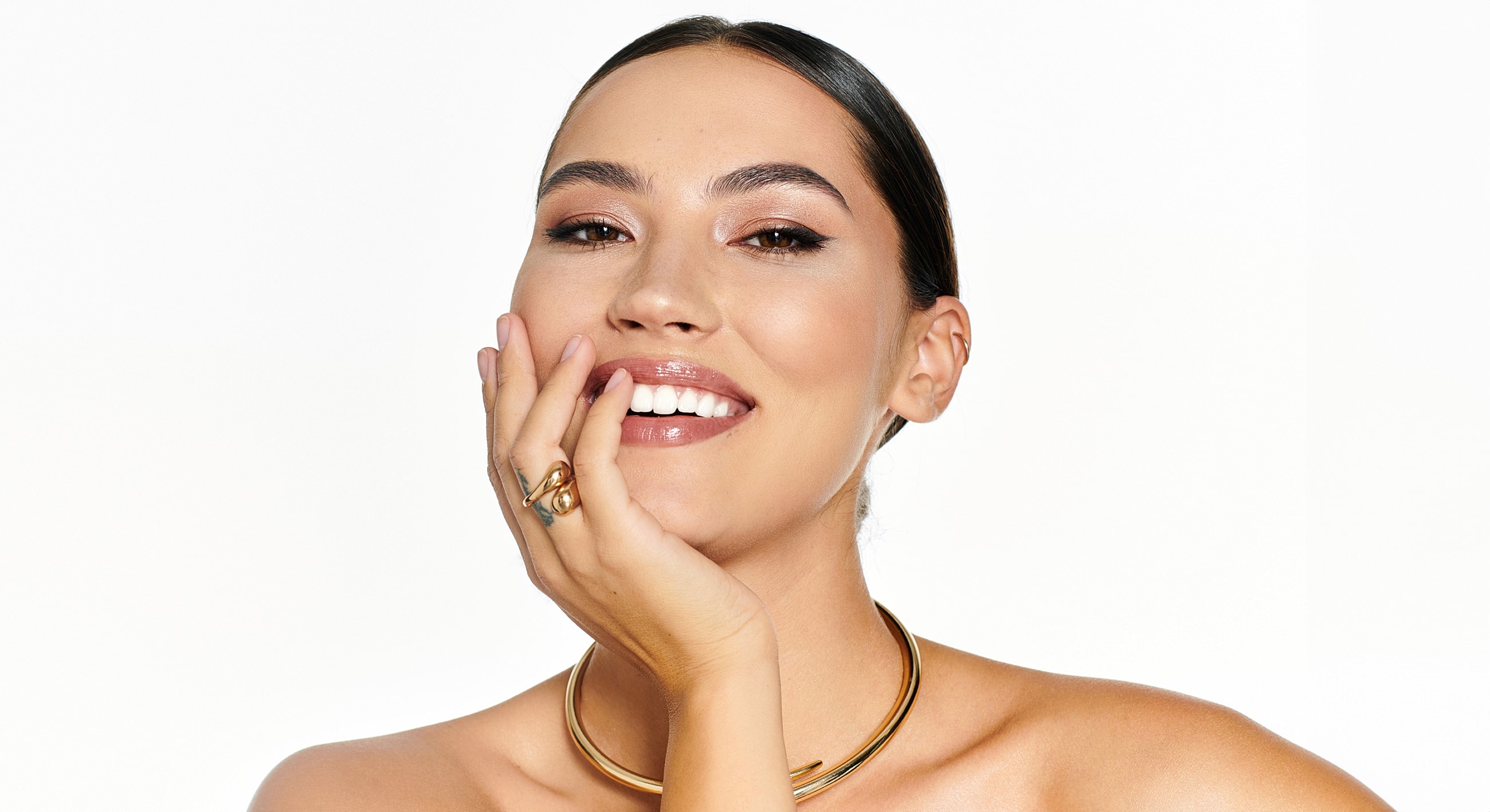 Smiling woman showcasing jewelry, with natural makeup.