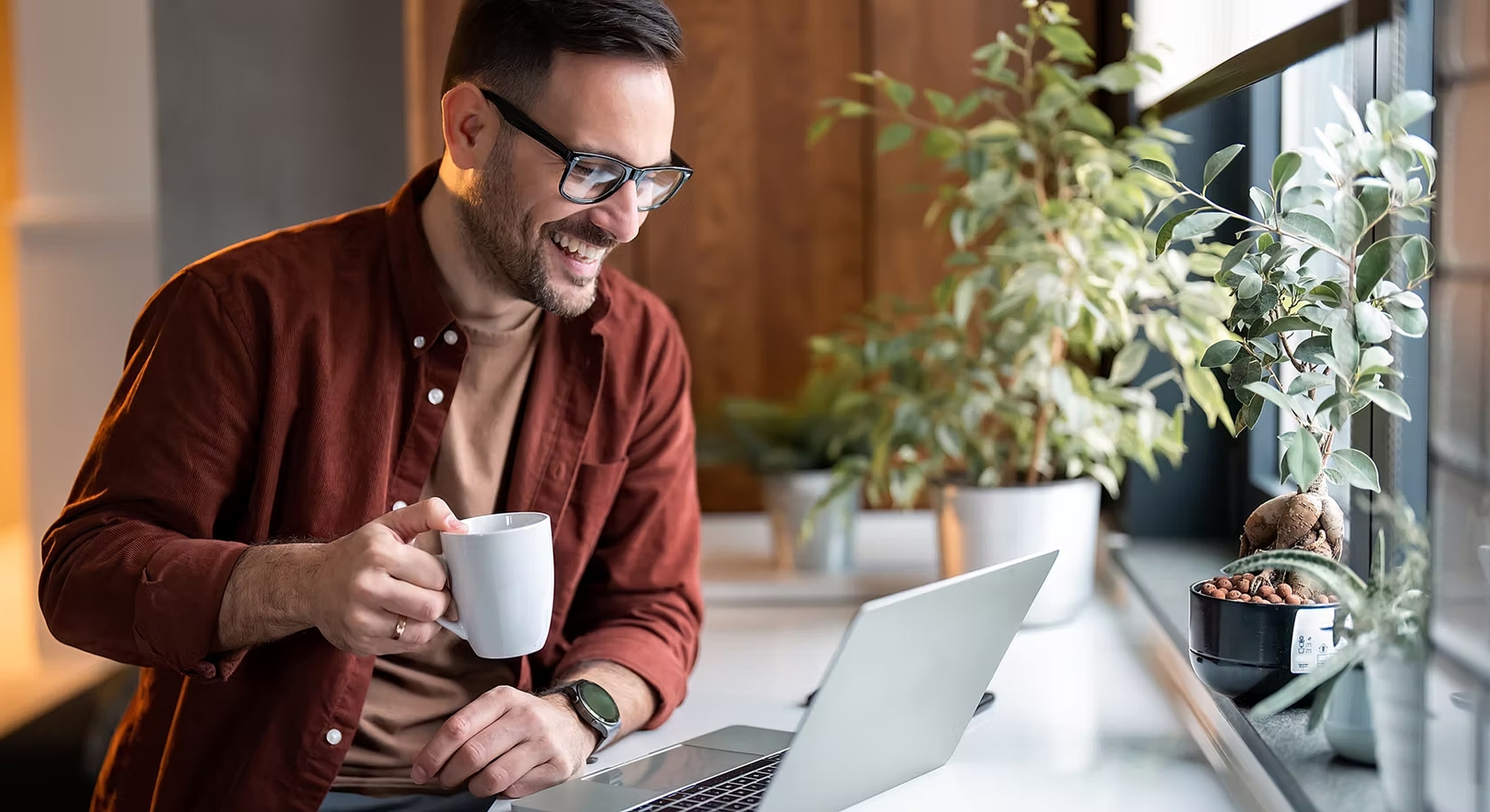 Man enjoying coffee while working on laptop.
